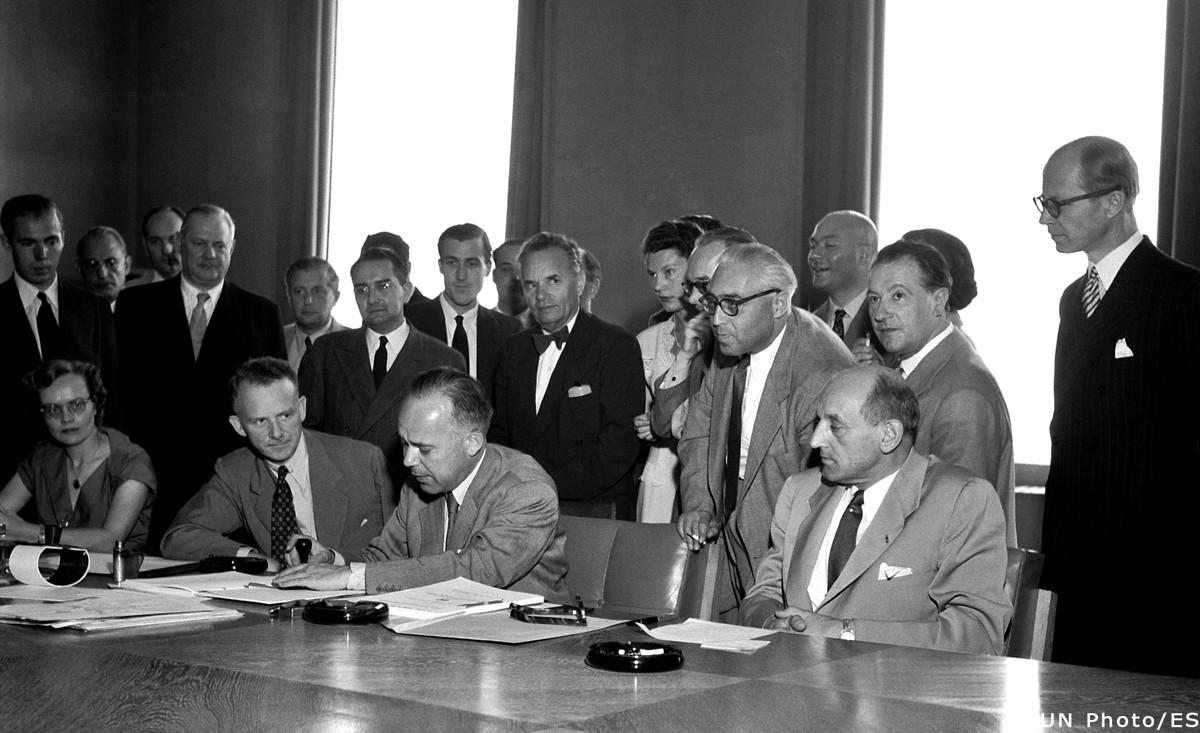 Unterzeichnung der Genfer Flüchtlingskonvention am 1. August 1951. Sitzend, v.l.n.r.: John Humphrey (Kanada), Direktor der Abteilung für Menschenrechte der Vereinten Nationen; Knud Larsen (Dänemark), Präsident der Konferenz; Gerrit Jan van Heuven Goedhart (Niederlande), Hoher Kommissar für Flüchtlingsfragen. (Quelle: Arni/UN Archives)